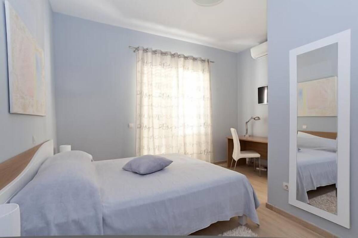 Un dormitorio con cama, escritorio, silla, espejo y ventana con cortinas.