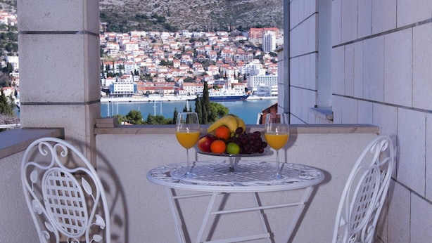 A balcony with two white metal chairs and a small round table, featuring a fruit and juice arrangement. - Sunflower Apartment (Dubrovnik)