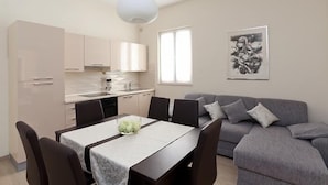 A modern kitchen with white cabinets, a dining table with chairs, and a gray sofa. - Sunflower Apartment (Dubrovnik)
