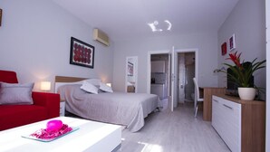 A modern hotel room with a bed, a desk, a chair, a TV, and a plant. - Sunflower Apartment (Dubrovnik)