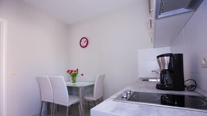 A compact kitchen with a dining table, chairs, a coffee maker, and a clock on the wall. - Sunflower Apartment (Dubrovnik)