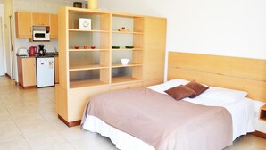 Hotellihuone, jossa on sänky, puinen vaatekaappi, pieni keittiönurkkaus, jossa on mikroaaltouuni, sekä jääkaappi.
