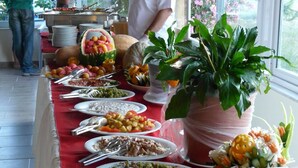 A buffet table with various dishes and utensils, surrounded by potted plants and a window with a view of greenery. - Safak Beach Motel (Manavgat)