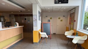 Hotellin vastaanottoalue, jossa on palvelutiski, tuoleja, taulu ja ikkuna.