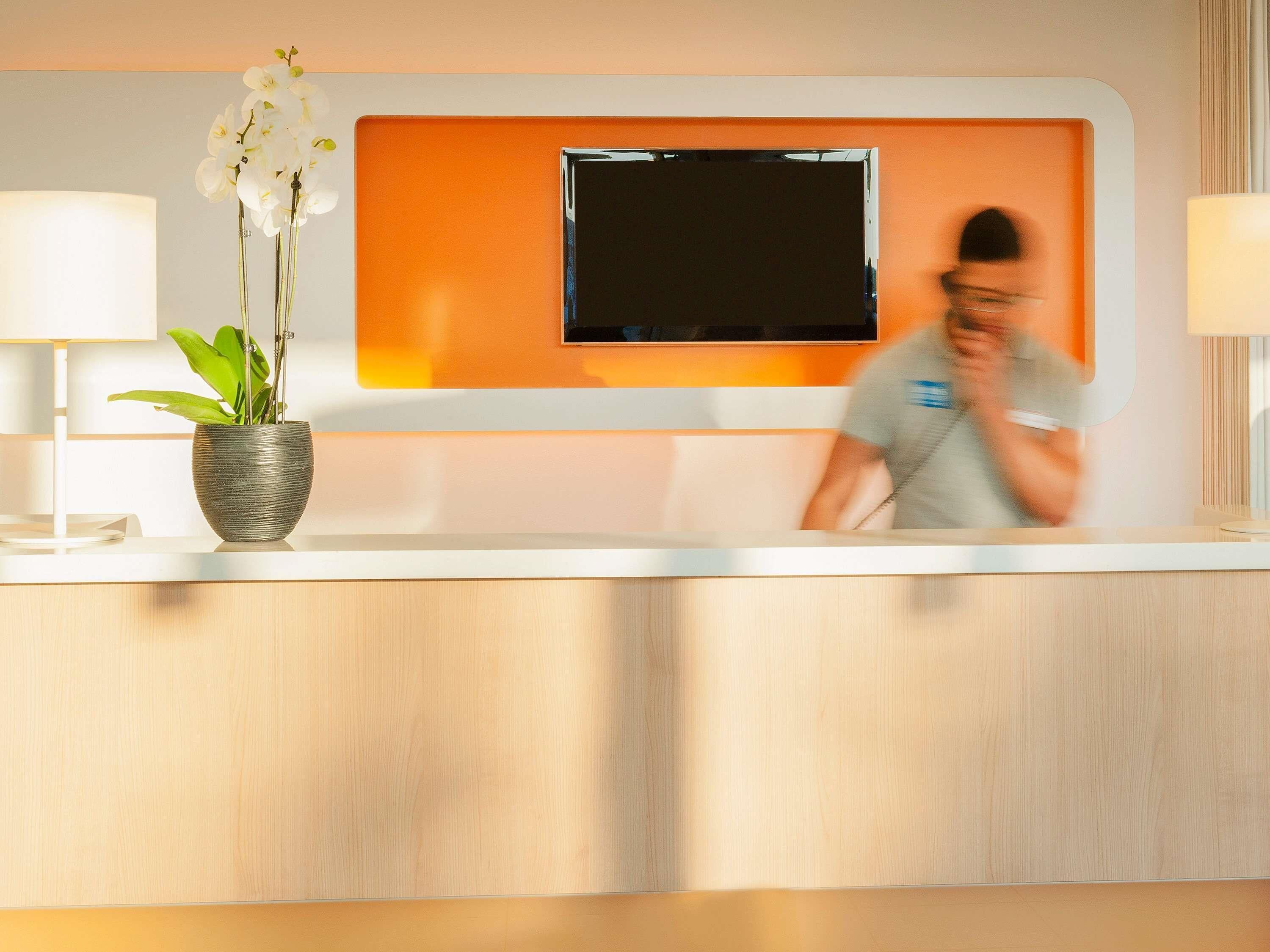 Taulell de recepció amb televisió de pantalla plana, una planta en test i una làmpada.