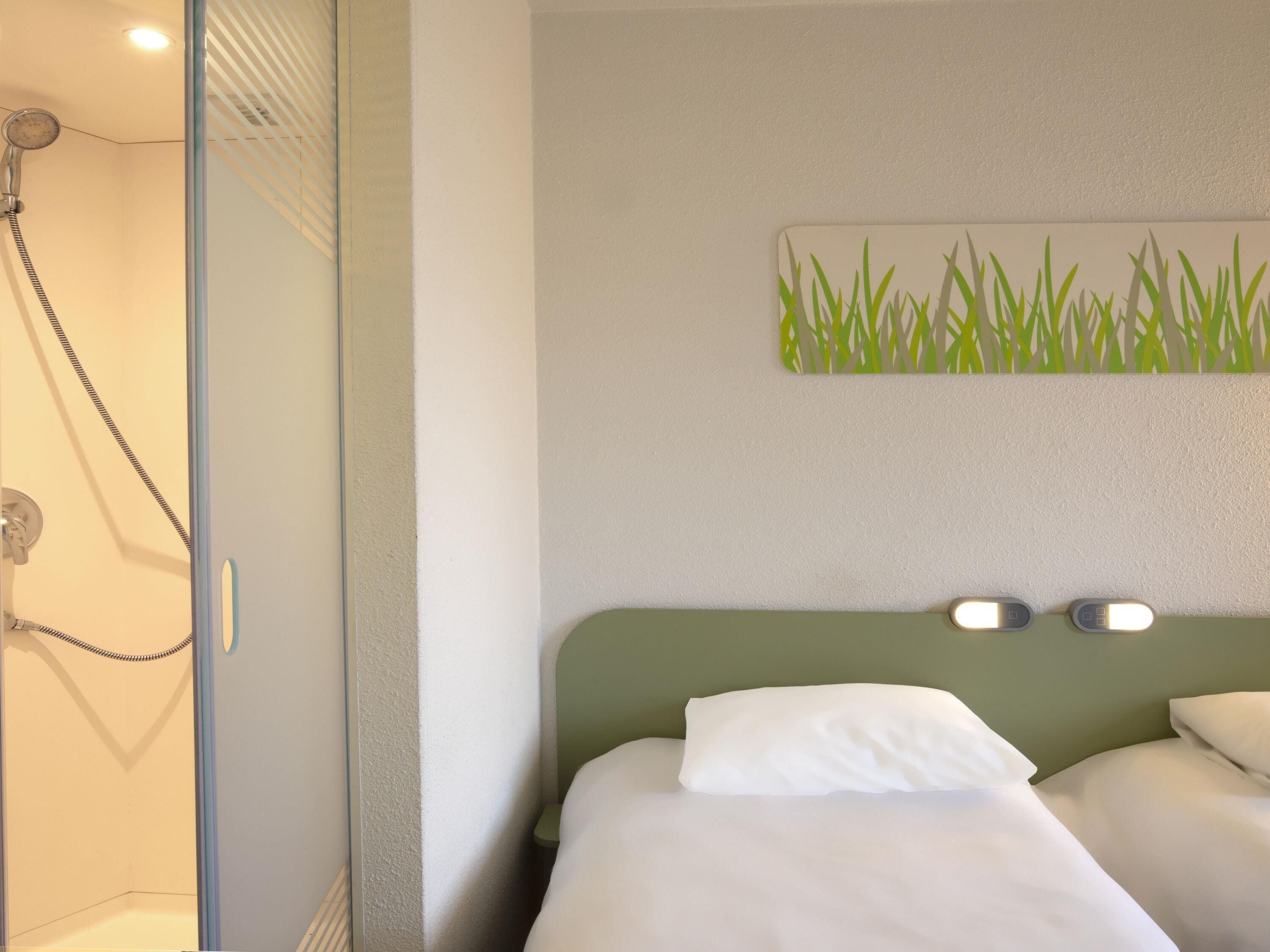 Una habitación de hotel con ducha, una cama con ropa de cama blanca y un aplique de pared.