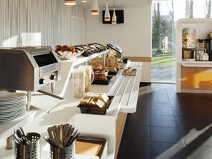 A breakfast buffet with various food items, a coffee machine, and a view of the outdoors. - ibis budget Antwerpen Port (Antwerp)
