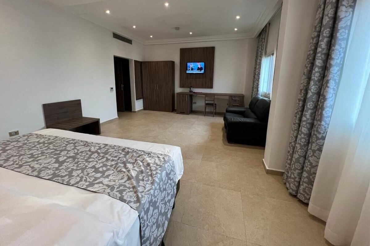 Ett rymligt hotellrum med en stor säng, ett skrivbord, en TV och en sittgrupp.