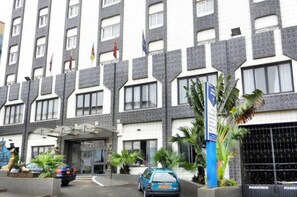 A multi-story hotel with a modern facade, featuring a parking area and a sign indicating a parking fee. - Minotel Franco (Yaoundé)