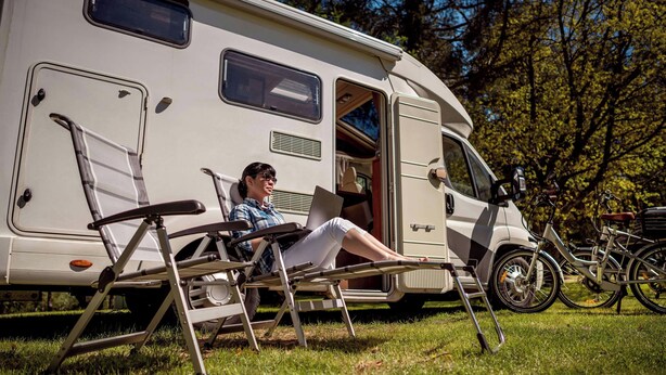 Une personne se détend dans un fauteuil à l’extérieur d’un camping-car, avec un vélo garé à proximité.