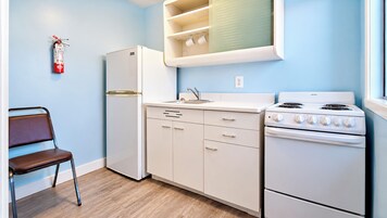 Una cocina compacta con refrigerador, estufa, pileta y una silla.
