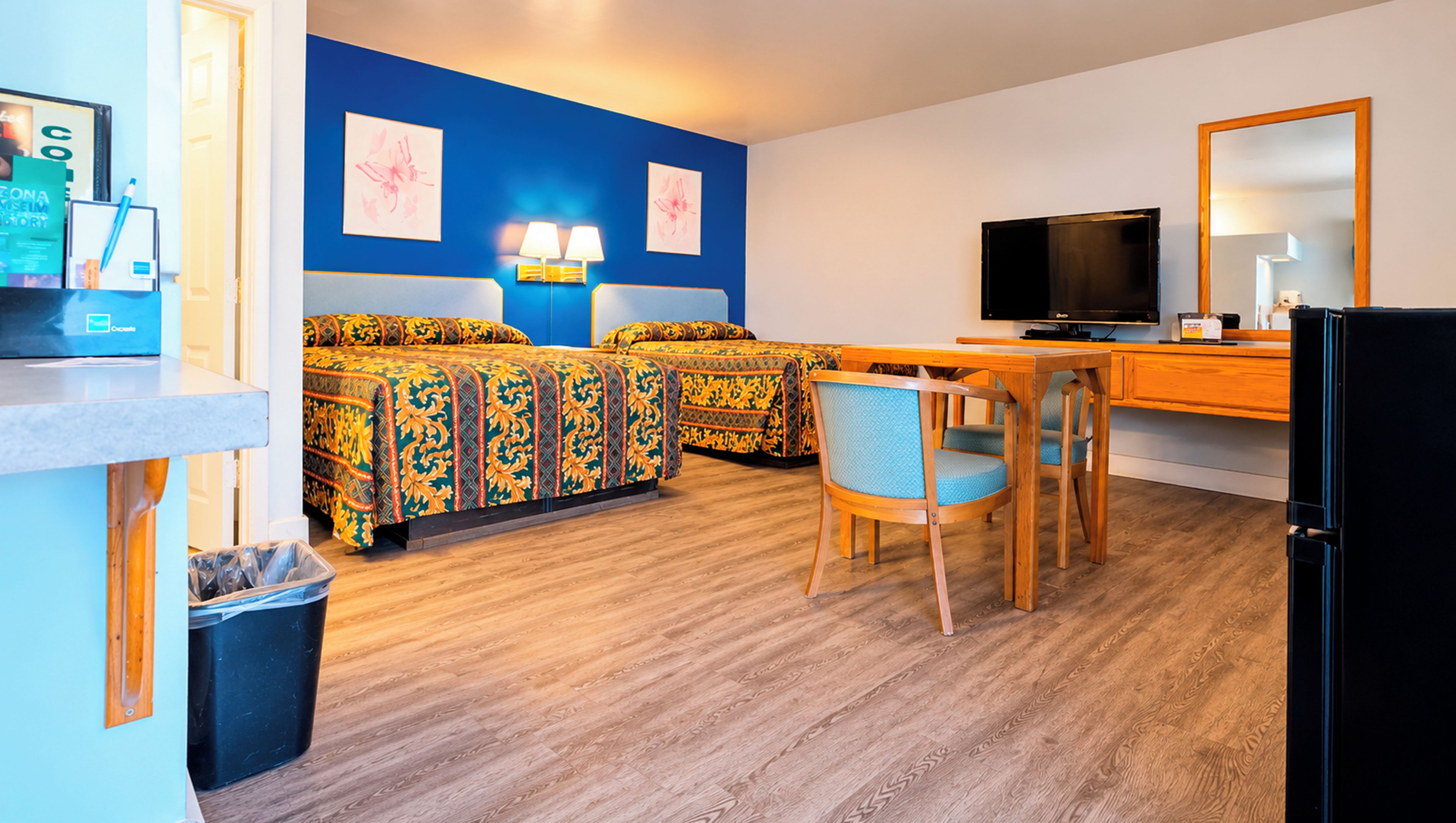 Habitación de hotel con cama, escritorio, silla, televisor y un cesto de basura.