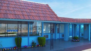 Un bâtiment avec un toit recouvert de tuiles rouges, des murs extérieurs bleus et une fenêtre sur laquelle on peut lire le mot « BUREAU ».