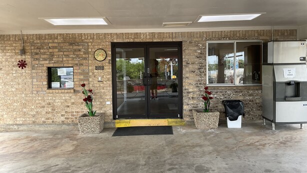 A building entrance with a brick wall, a glass door, a clock, and a water dispenser. - Glen Rose Inn and Suites (Glen Rose)