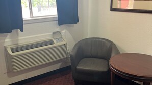 A room with a window, a radiator, a grey armchair, and a round table. - Glen Rose Inn and Suites (Glen Rose)