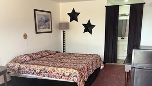 A hotel room with a bed, a desk, a lamp, and a mirror. - Glen Rose Inn and Suites (Glen Rose)