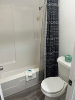 Bañera con ducha, jabón, shampoo, papel higiénico