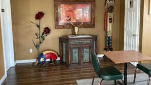 A dining area with a wooden table and chairs, a decorative cabinet, a framed painting, and a Native American figure. - Glen Rose Inn and Suites (Glen Rose)