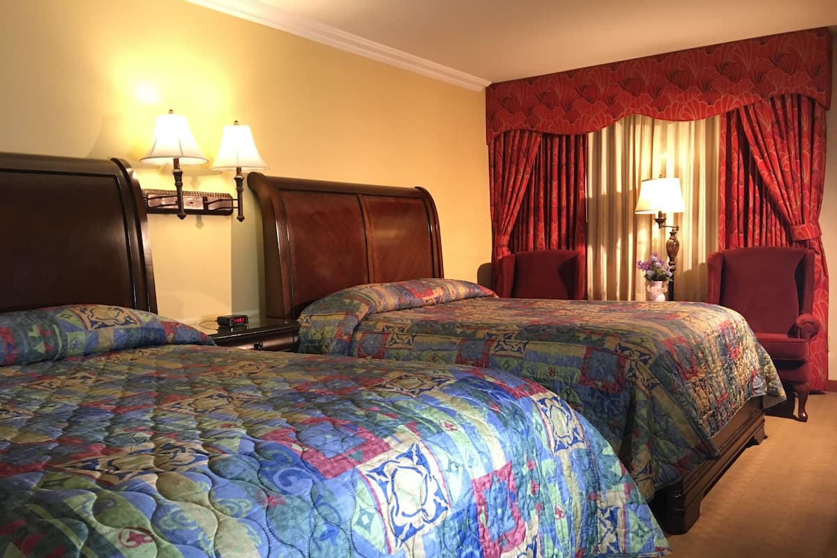 A hotel room with two beds, each with a patterned bedspread, a wooden headboard, a nightstand with a lamp, and a chair.
