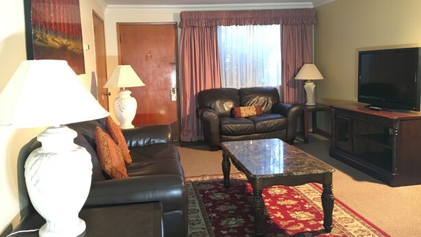 A living room with a sofa, a coffee table, a TV, and two lamps. - Acorn Motor Inn (Oak Harbor)