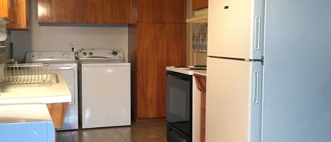 A kitchen with wooden cabinets, a white refrigerator, a stove, and a washing machine.