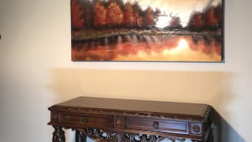 Une pièce décorée d’un grand tableau représentant une scène de forêt, d’une console en bois et d’un tapis à motifs.
