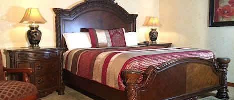 A traditional four-poster bed with a wooden headboard, flanked by two nightstands with lamps, a wooden chair, and a patterned carpet.