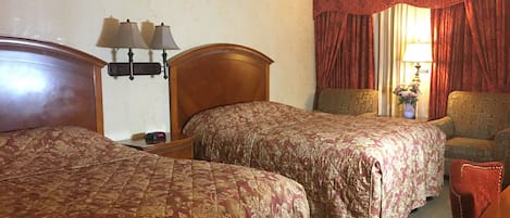 Habitación de hotel con dos camas, una mesita de noche con lámparas, una silla y un ventanal con cortinas.