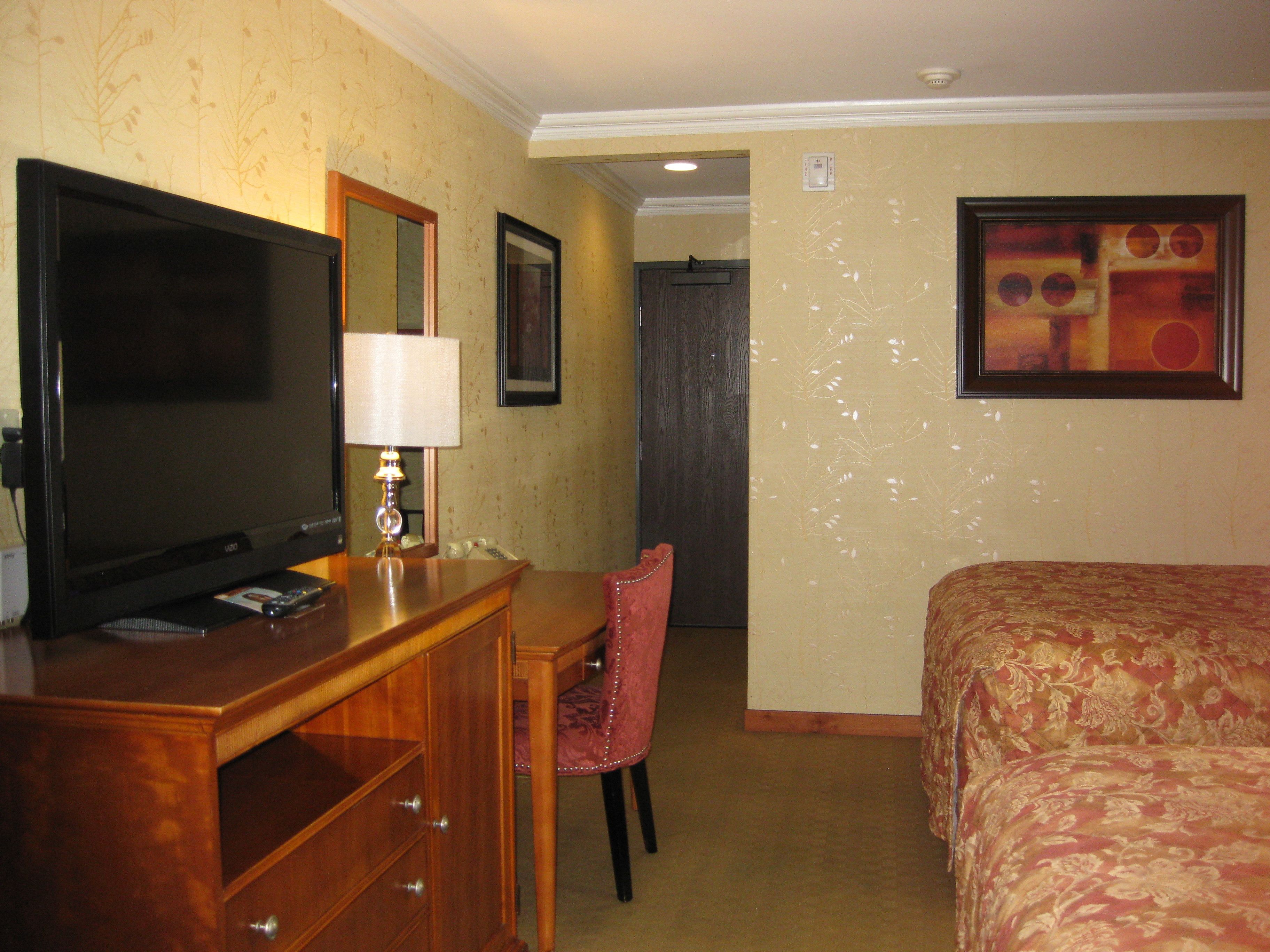 A hotel room with a bed, a desk with a television, a chair, and a painting on the wall.