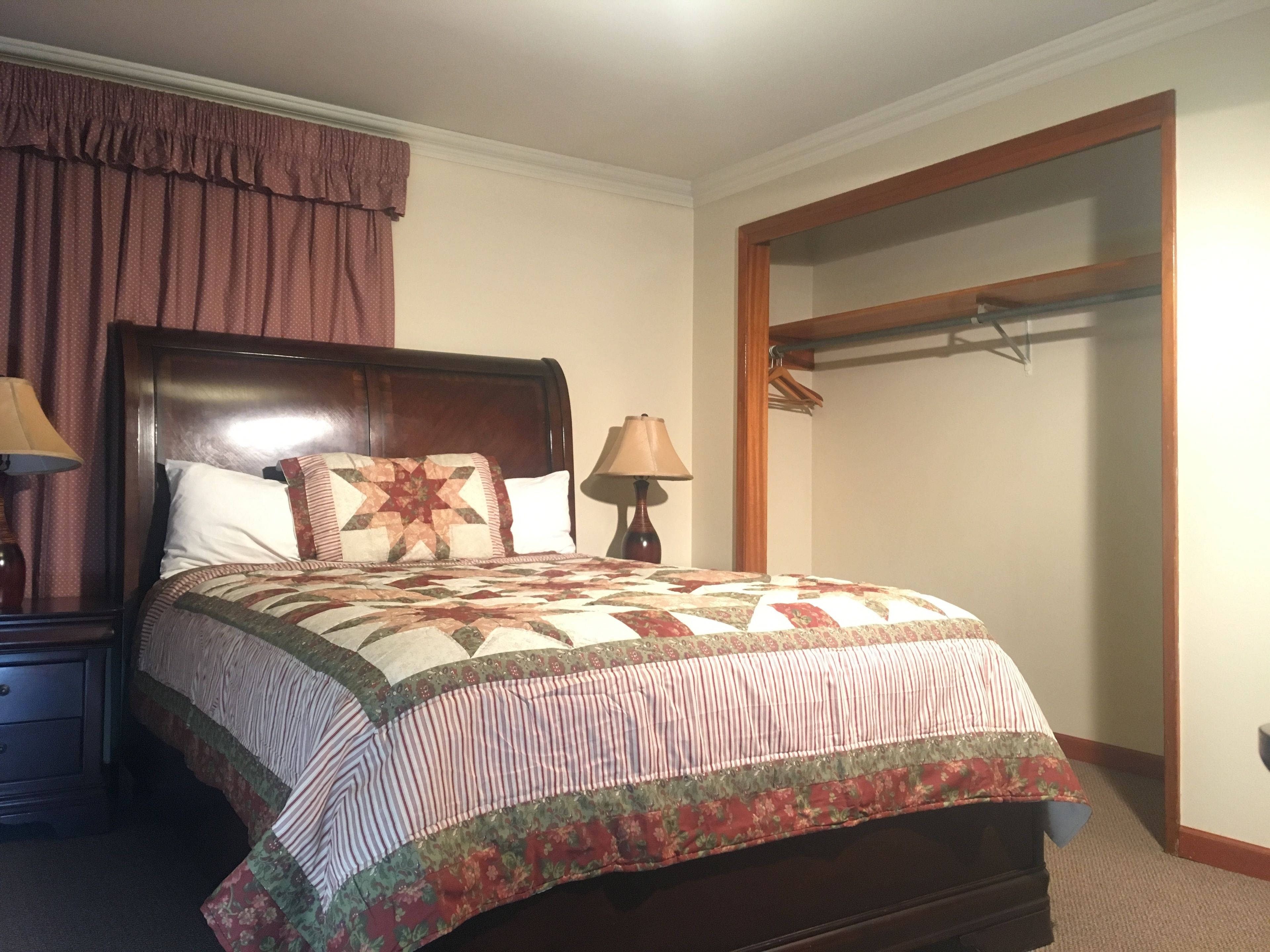 A neatly made bed with a floral quilt, a wooden headboard, a bedside lamp, and a wooden nightstand with a drawer.