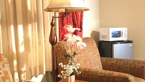 A hotel room with a sofa, a table with a lamp, a vase with flowers, and a microwave on a small table. - Acorn Motor Inn (Oak Harbor)
