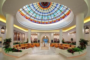 A spacious lobby with a large, colorful stained glass dome ceiling, seating areas, and a central fountain. - Hilton Marsa Alam Nubian Resort (Marsa Alam)