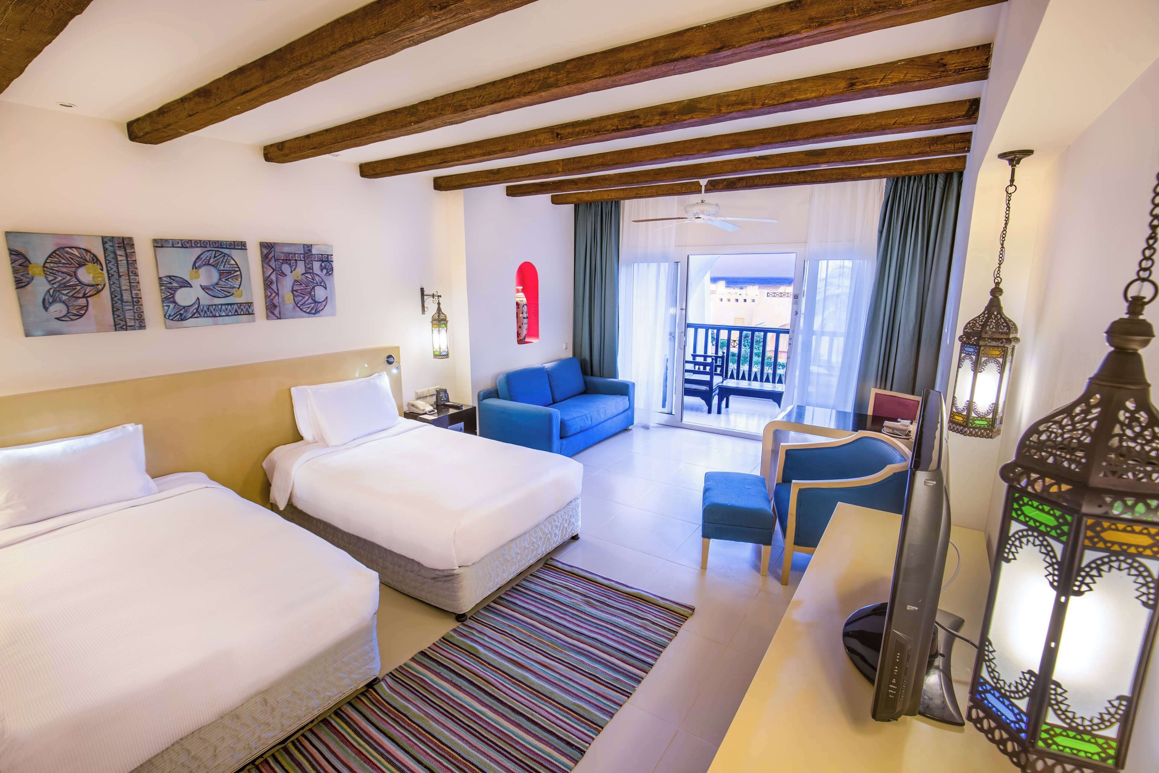 A hotel room with two beds, a sofa, a desk, and a view of the outside.