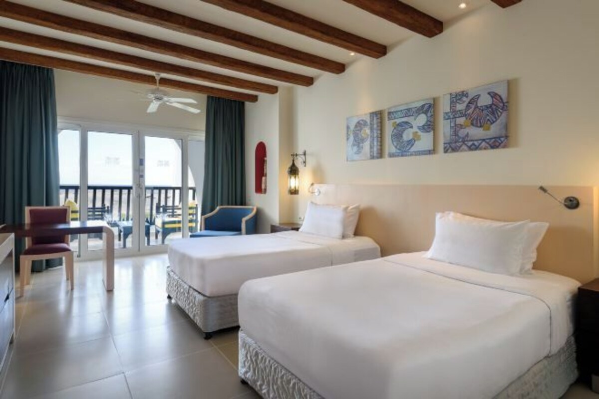 A hotel room with two beds, a desk, a chair, and a balcony with a view.