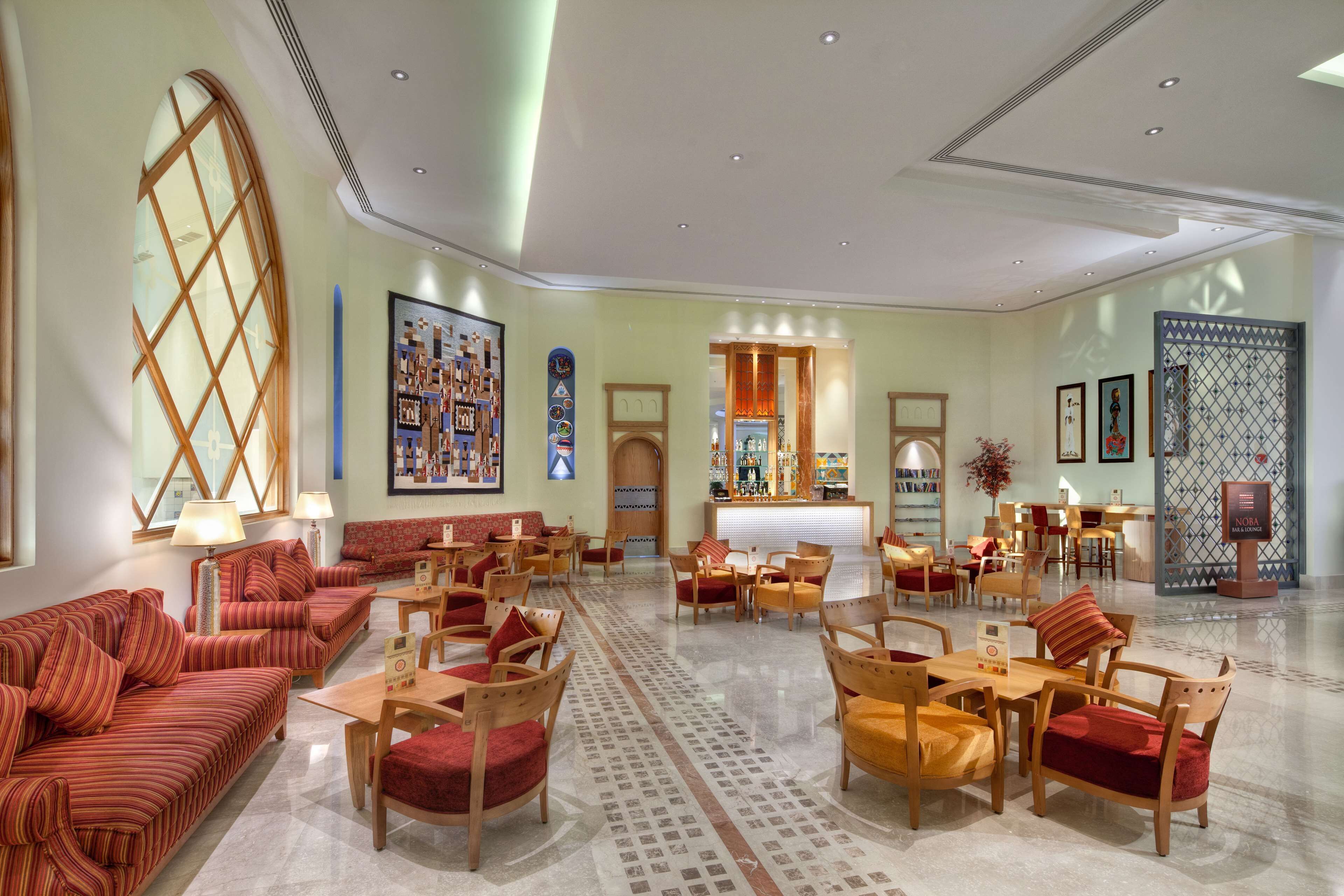 A spacious lobby with red upholstered sofas, wooden chairs, and a central bar area.