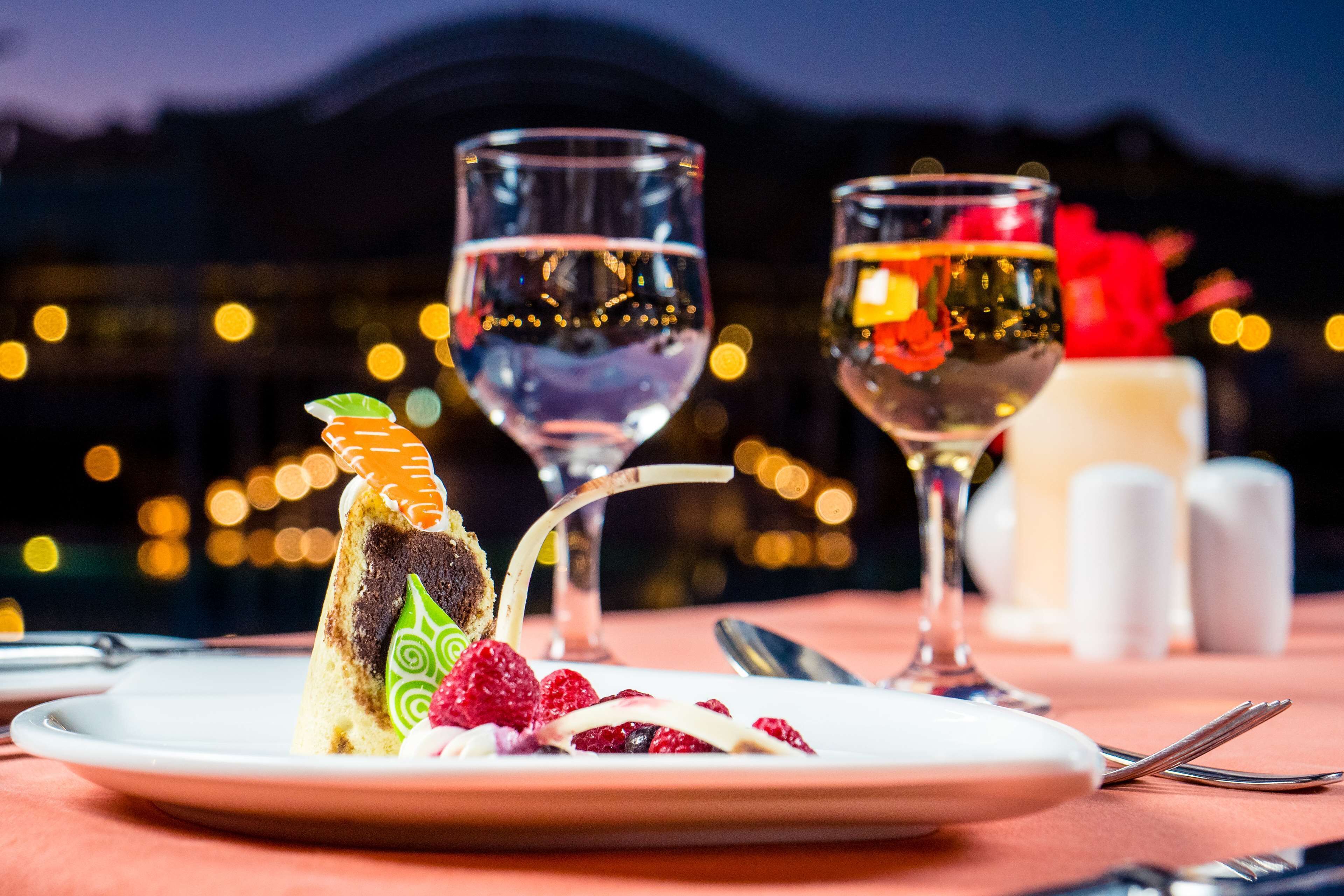 A dessert plate with a slice of cake and berries, two wine glasses, and a table setting with a fork and knife.