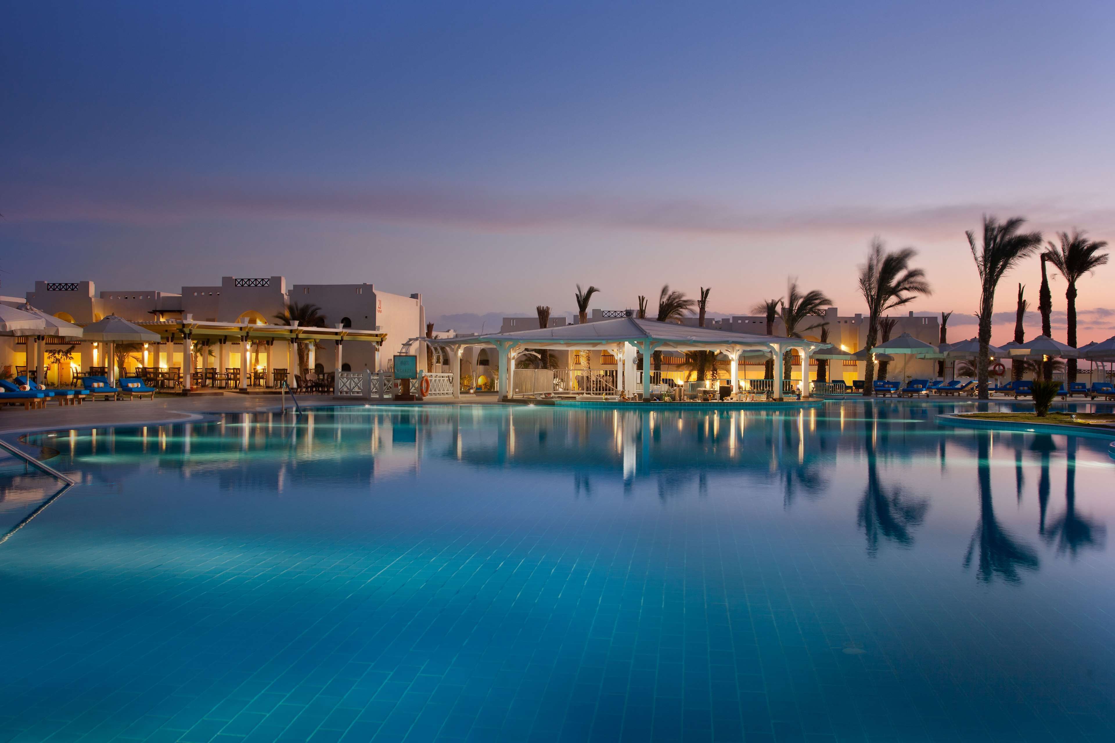 A pool area with lounge chairs and umbrellas, surrounded by buildings with distinct architectural features.