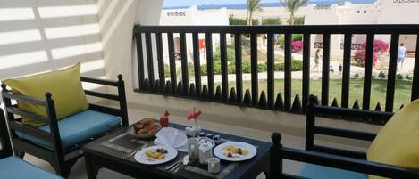 Varanda com mesa posta para café da manhã, vista para uma praia e palmeiras.