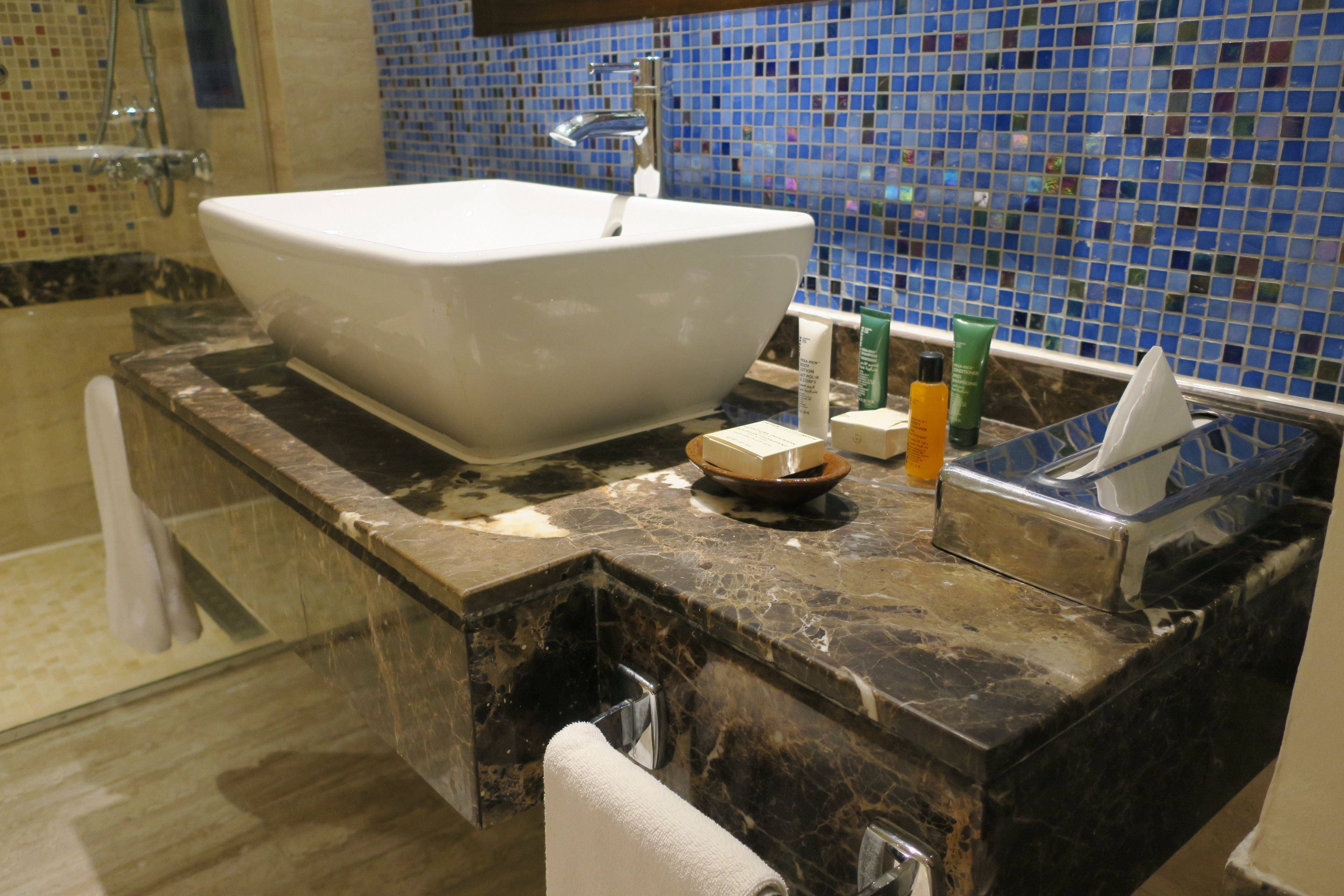 Un baño con lavamanos blanco, espejo y pared de mosaico azul.