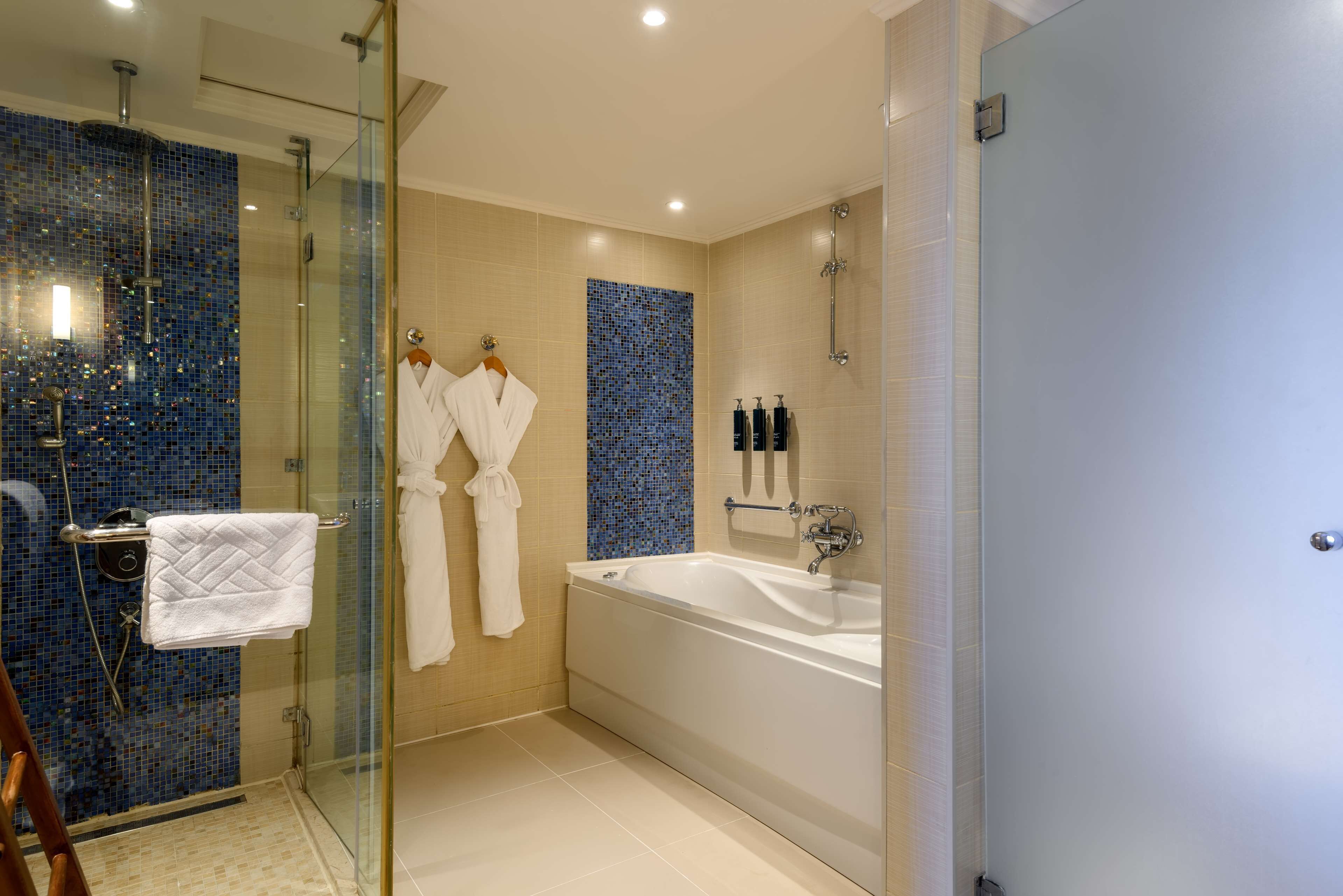 A modern bathroom with a glass-enclosed shower, a large bathtub, and two white towels hanging on hooks.