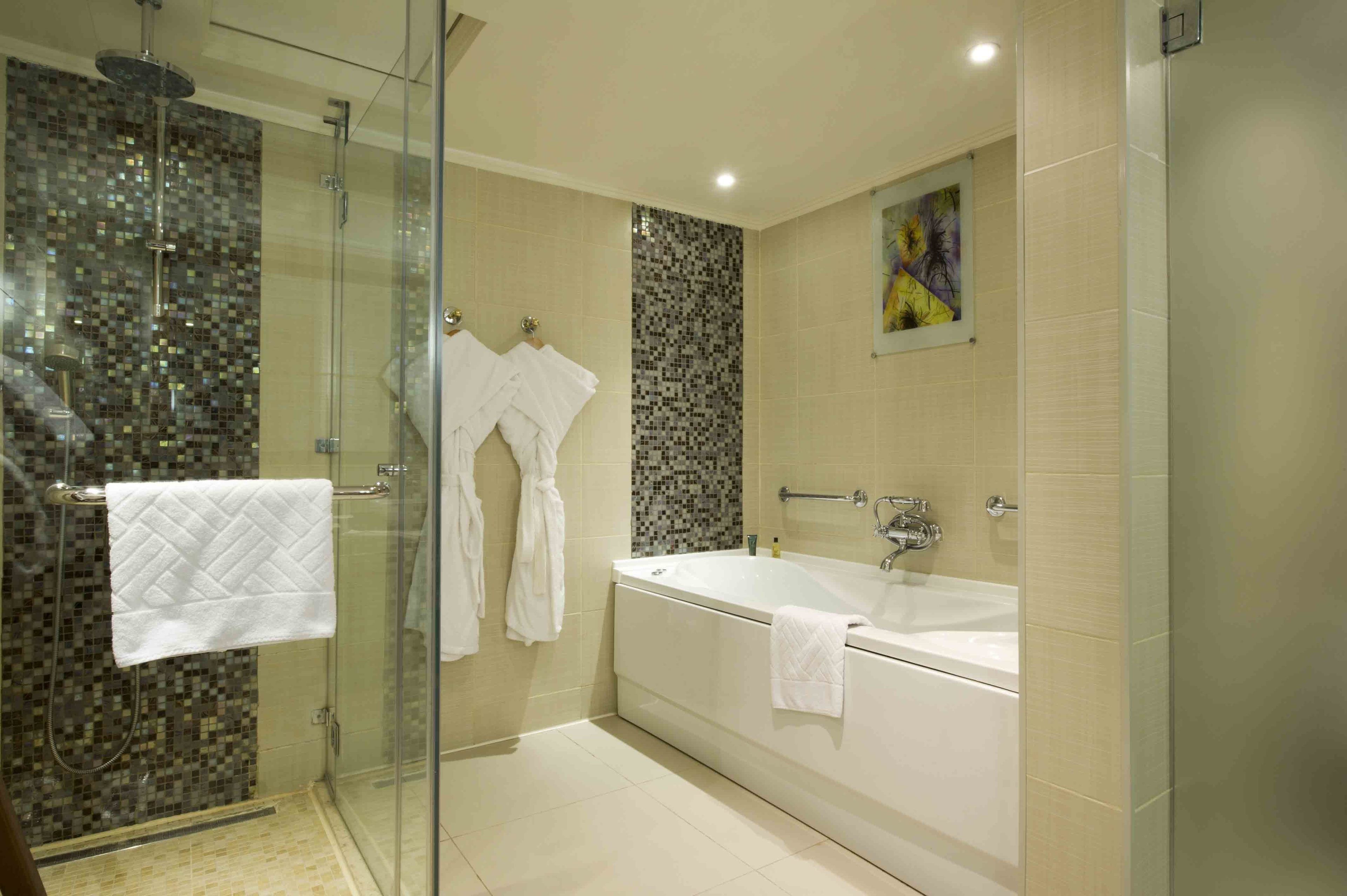 Un baño moderno con cabina de ducha de vidrio, una bañera independiente y un muro de mosaicos.