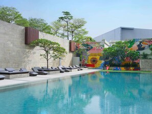 Una piscina con sillas de descanso, un mural y árboles.