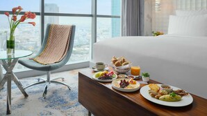 Een hotelkamer met een bed, een ontbijttafel, een stoel en uitzicht op de stad.