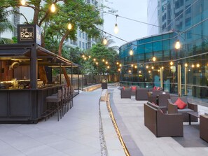 An outdoor seating area with tables and chairs, a bar, and a sign that reads 'The Box'. - Pullman Jakarta Central Park (Jakarta)