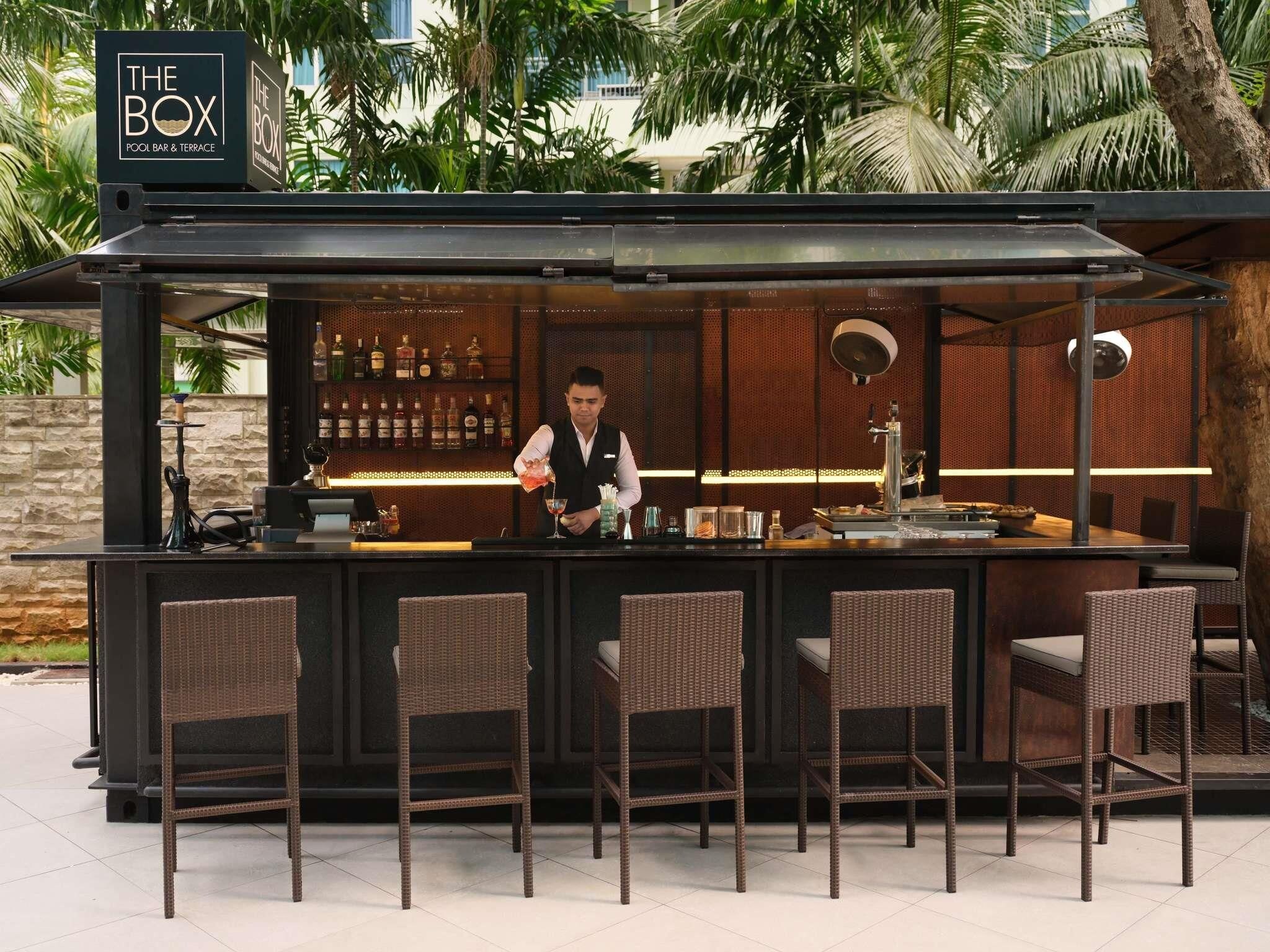 A bar area with a sign reading 'The Box' and a bartender preparing a drink.