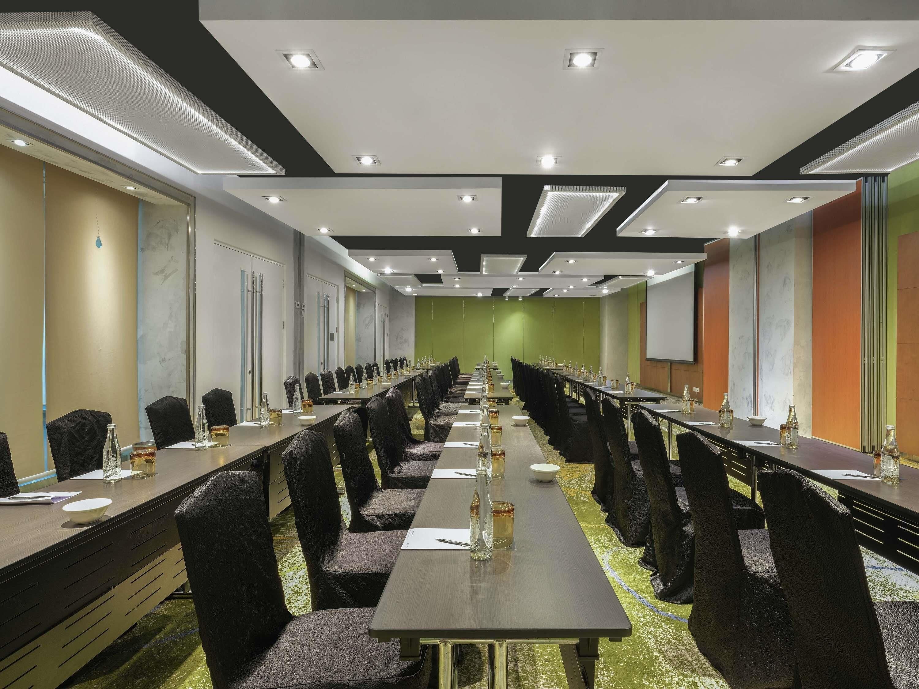 Una sala de conferències amb taules llargues, cadires i una pantalla projectora.