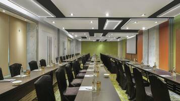 Una sala de conferències amb taules llargues, cadires i una pantalla projectora.