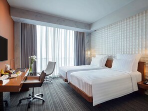 Habitación de hotel con dos camas, un escritorio, una silla, televisión y un ventanal con cortinas.
