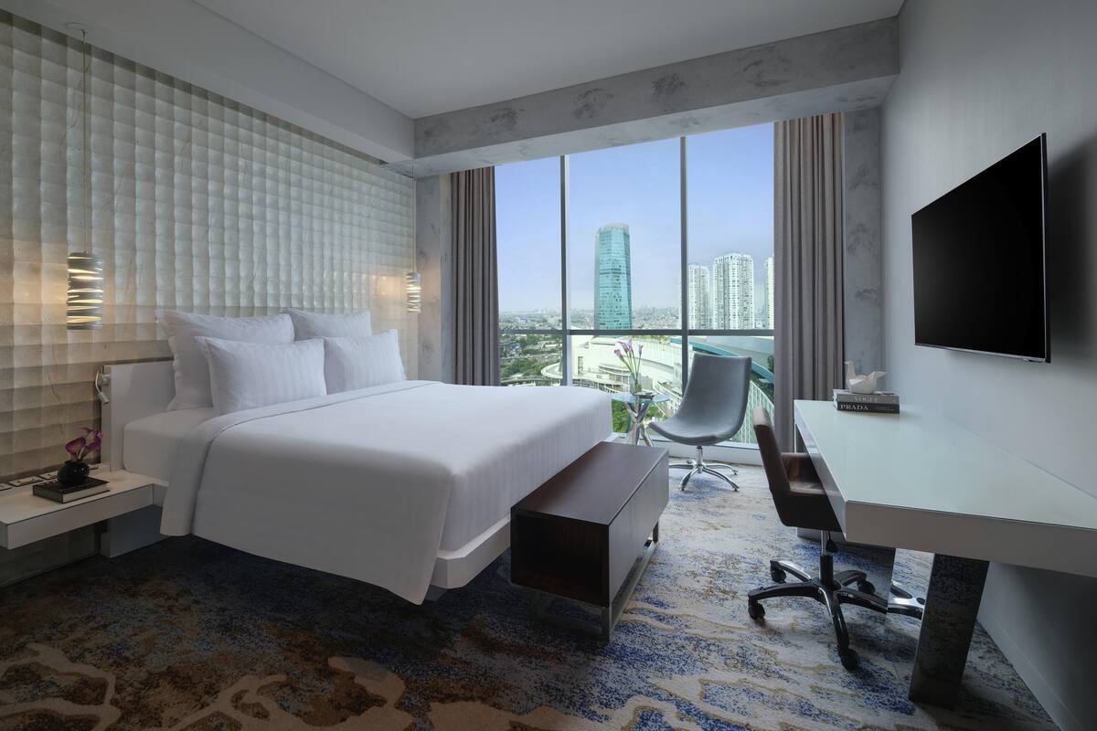 A modern hotel room with a large bed, a desk, a chair, and a TV.