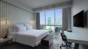 A modern hotel room with a large bed, a desk, a chair, and a TV.